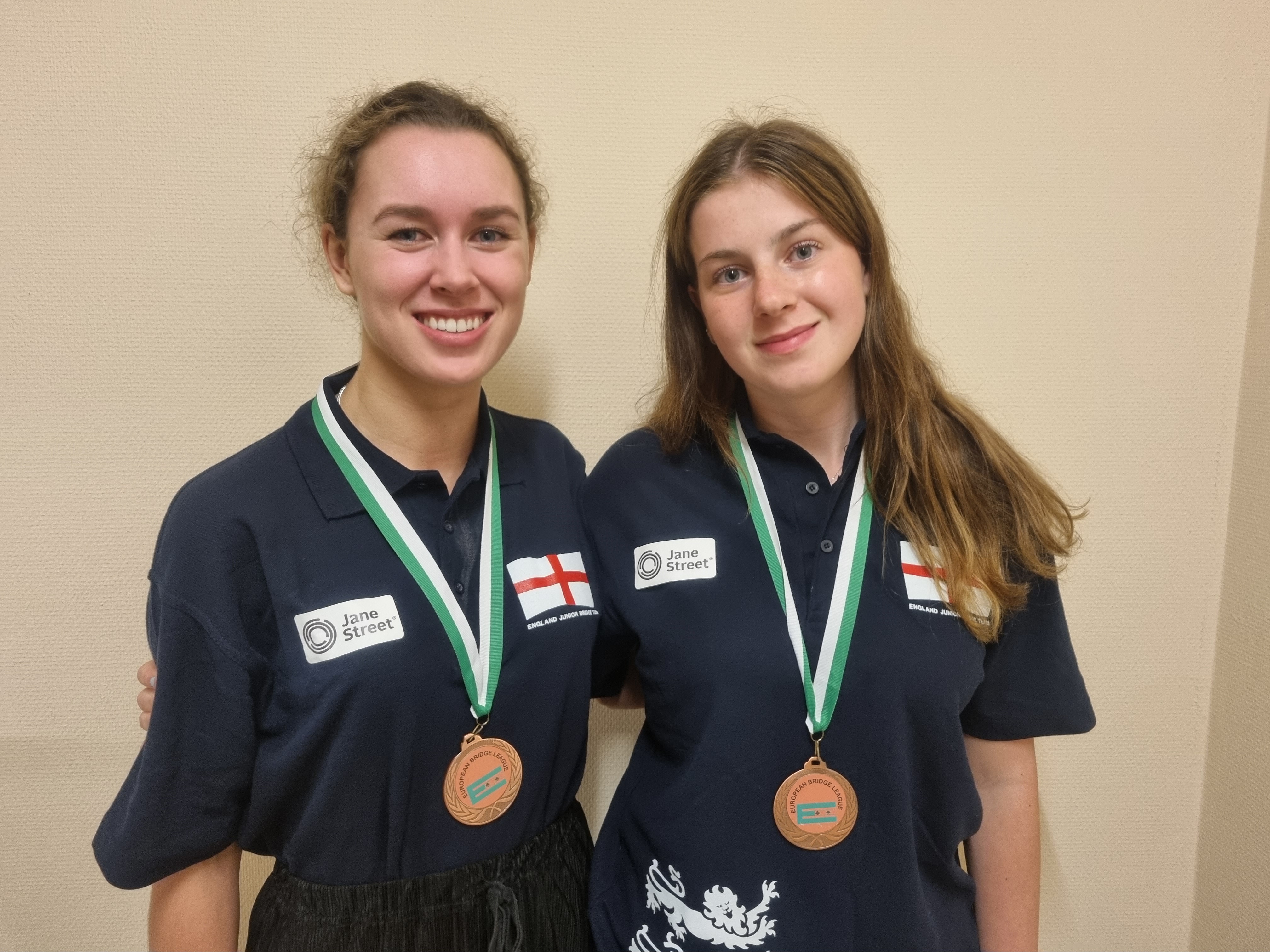 Bridge players Lottie and Imogen from the England U26W youth squad are smiling at the camera and wearing their bronze medals